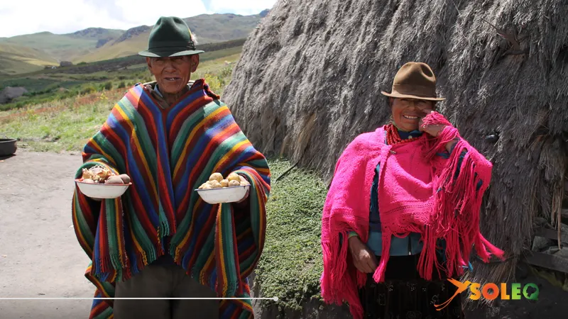 Pareja indígena con vestimenta tradicional ofreciendo alimentos en los Andes ecuatorianos.