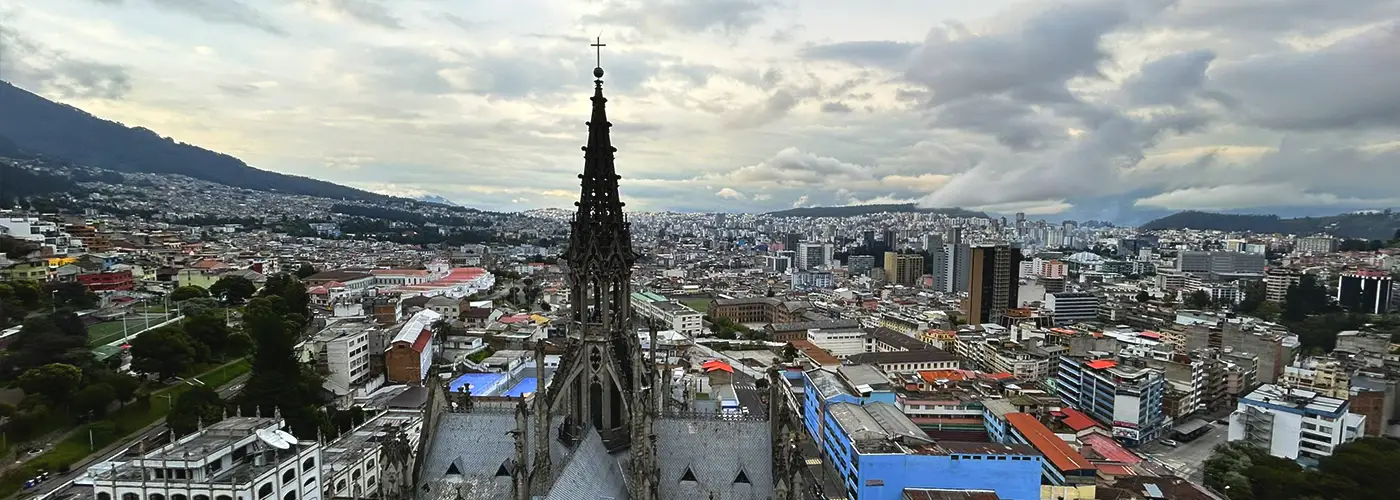 Vista desde la Basílica del Voto Nacional con panorámica del norte de Quito y su paisaje urbano moderno bajo un cielo nublado.