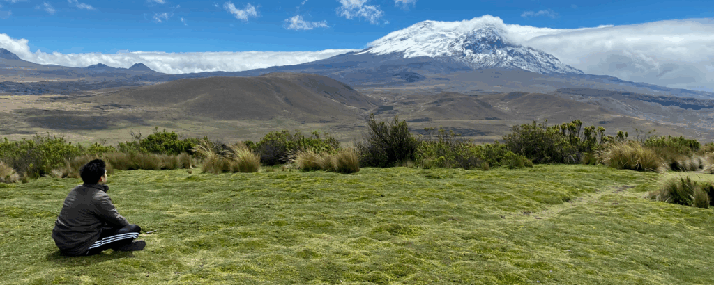 View of Antisana Volcano in Ecuador with a traveler meditating in front of its snow-capped peak