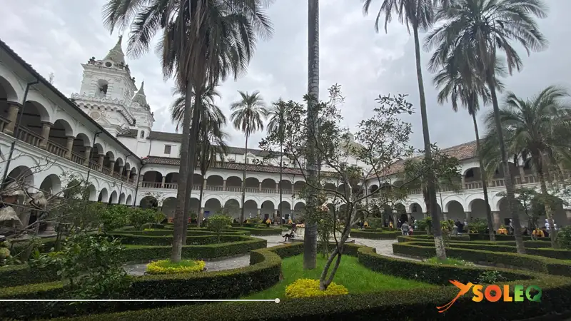 Patio interior del Convento de San Francisco en Quito – un claustro colonial con elegantes arcos, altas palmeras y jardines perfectamente cuidados.