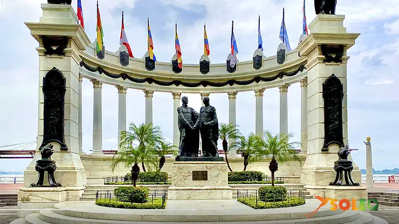 Monument to Simón Bolívar and San Martín on the Malecón 2000 in Guayaquil, surrounded by flags and palm trees.