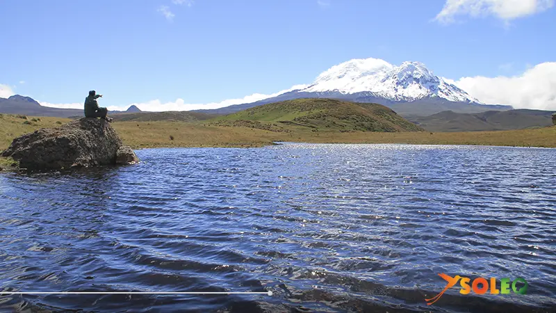 Tourist admiring the majestic Antisana Volcano and its turquoise lagoon on a clear day in Ecuador’s Andes.