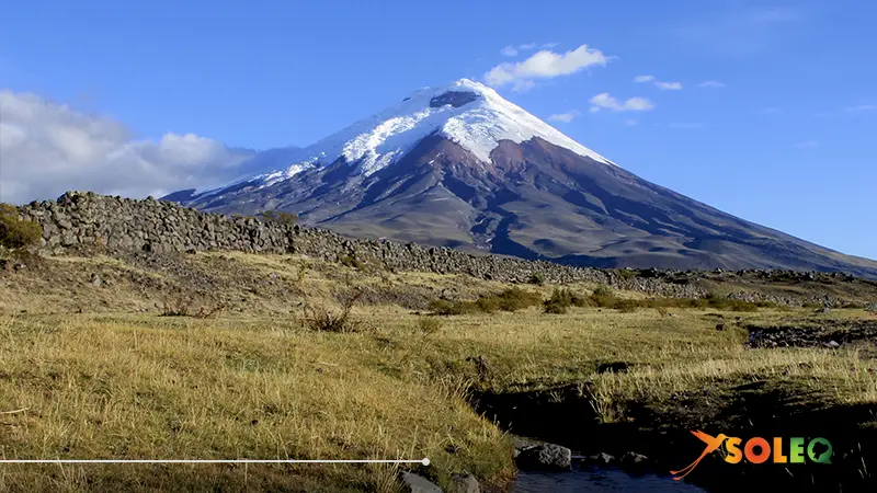 A breathtaking view of Cotopaxi Volcano under a clear blue sky, with hikers exploring the trails of Cotopaxi National Park.