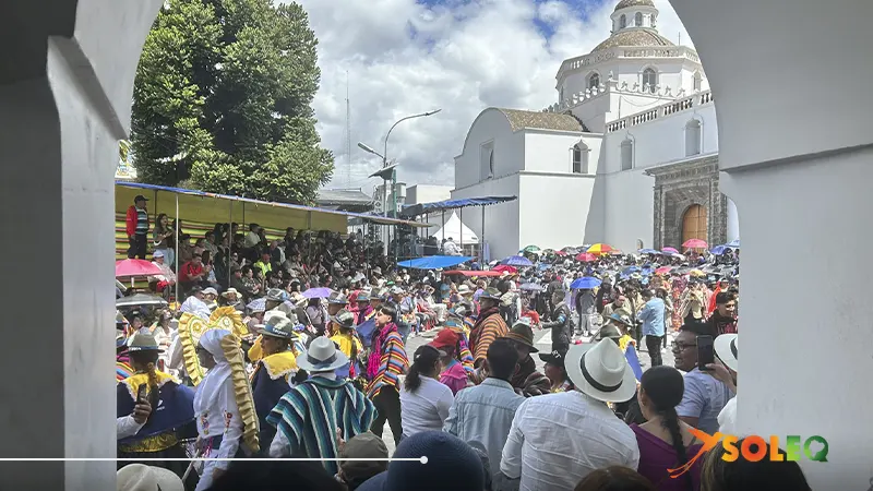 Crowd and colorful parade of the Mama Negra festival in front of a historic church in Latacunga, Ecuador.