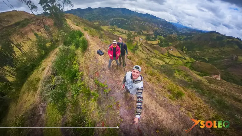 Tres excursionistas se hacen un selfie en un estrecho sendero de montaña con vistas panorámicas al valle andino durante el segundo día de la ruta circular de Quilotoa, en Ecuador.