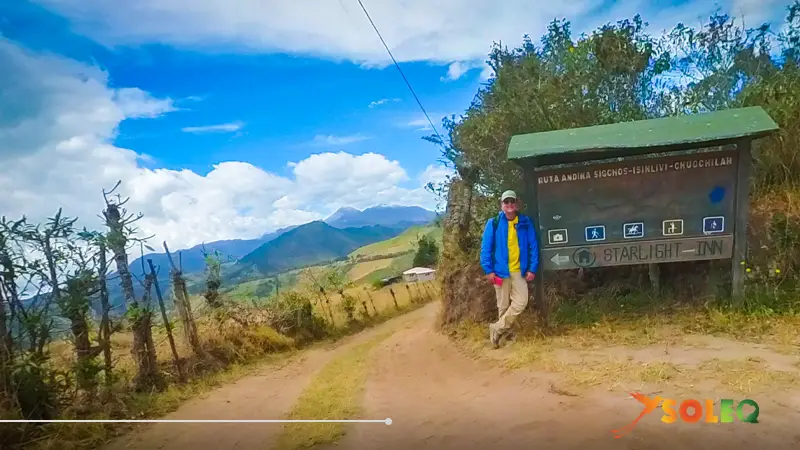 Un excursionista apoyado en una señal de madera que indica la ruta Sigchos-Isinlivi-Chugchilan en un camino de tierra durante la ruta circular de Quilotoa en Ecuador.