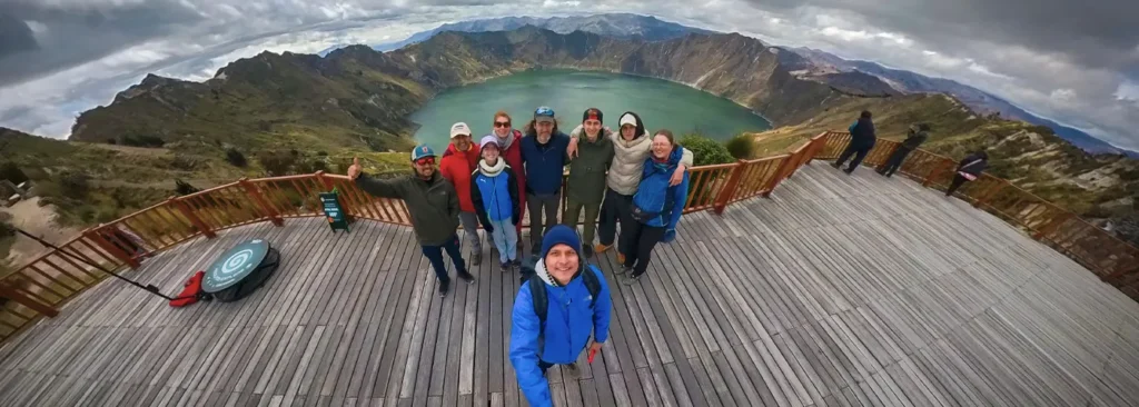 A group of hikers posing on the wooden Shalala viewpoint overlooking the turquoise Quilotoa crater lake during the Quilotoa Loop Trek in Ecuador.