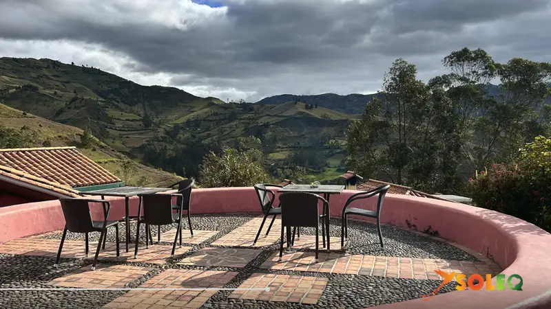 Una terraza al aire libre con mesas y sillas en un albergue de montaña con vistas a los valles andinos durante la ruta de senderismo del Circuito de Quilotoa en Ecuador.