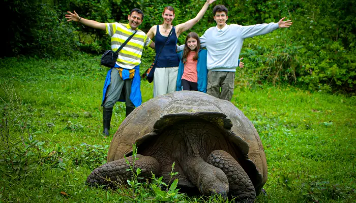Family posing with a giant Galápagos tortoise in a lush green natural habitat.