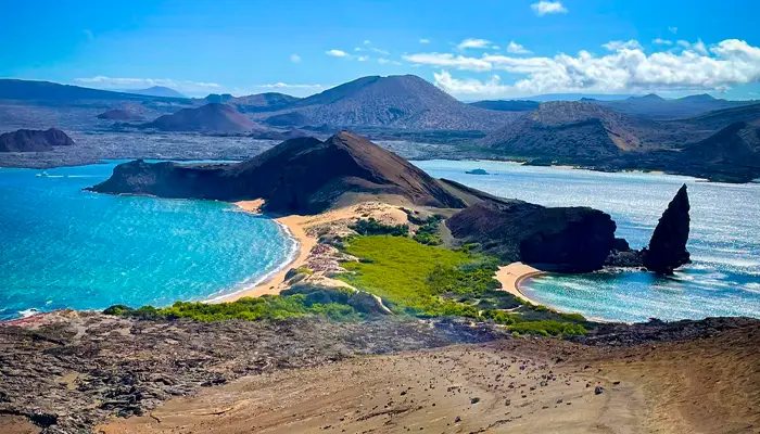 Vista panorámica de una isla de Galápagos con bahías turquesas, playas de arena, formaciones volcánicas y una formación rocosa distintiva en el océano.